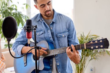 Sıradan kot ceketli sakallı esmer adam akustik gitar çalıyor, şarkı söylüyor.
