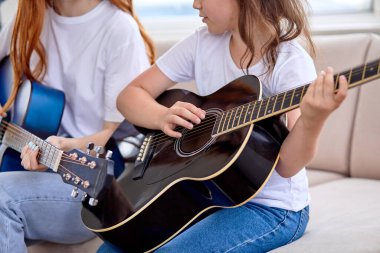 Küçük kızların akustik gitar çalarken, öğretmen kadınla otururken çekilmiş yakın plan fotoğrafı.