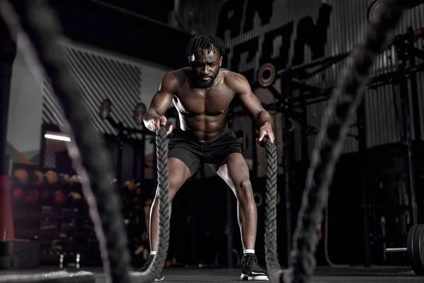 Deportista afroamericano haciendo ejercicios de cuerdas de batalla en el gimnasio crossfit. retrato —  Fotos de Stock