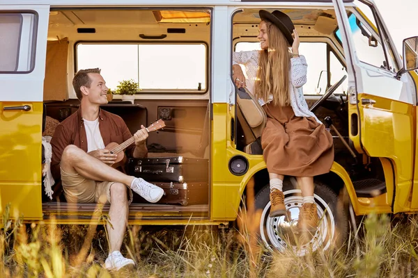 Gioiosa coppia hipster suonare la chitarra ukulele cantare una canzone in furgone giallo, in natura — Foto Stock