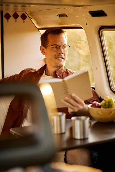 Caucasico ragazzo lettura libro mentre viaggiando in mini retro van, seduto dietro tavolo — Foto Stock