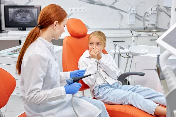 Красива біла дівчинка сидить на дивані, виглядаючи наляканим стоматологічним дрилем — стокове фото