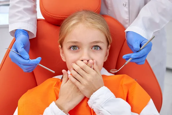 Налякана маленька дівчинка прикриває рот вручну під час лікування зубними інструментами в клініці — стокове фото
