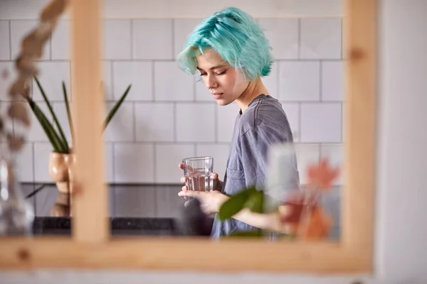 Csinos nő alkalmi ruhák állni néz le a konyhában, egy pohár vízzel — Stock Fotó