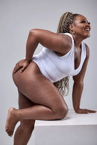 Plus size modelo sexy e feliz em bodysuit branco posando no cubo