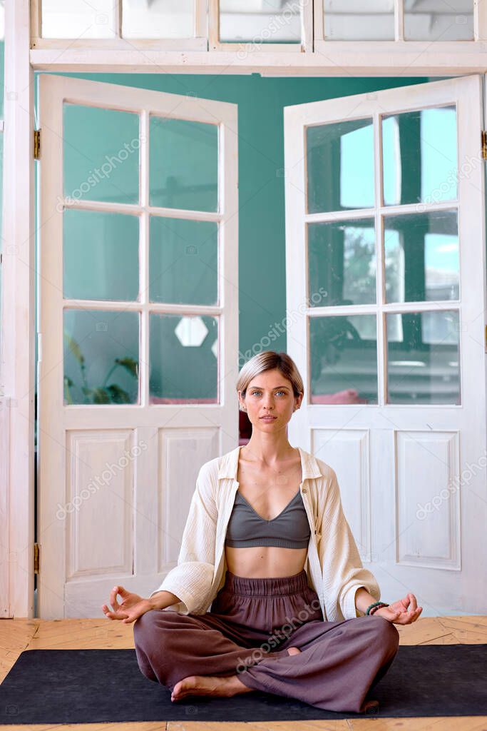 Young barefoot woman sitting on floor in Lotus pose and meditating
