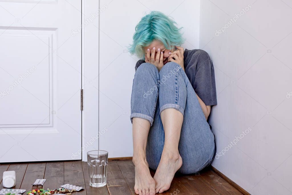 Suicide by medication overdose concept. pills on floor and young female with depression