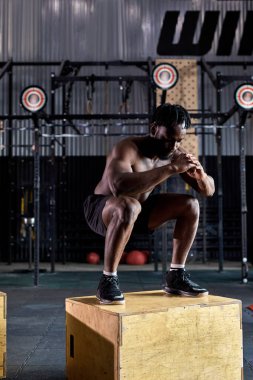 Formda olmayan Afrikalı sporcu spor salonunda plyometrik tahta kutuya atlıyor.
