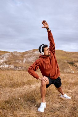 Motive olmuş zinde adam sahaya atlıyor, koşmadan önce bacaklarını esnetiyor, egzersiz yapıyor.