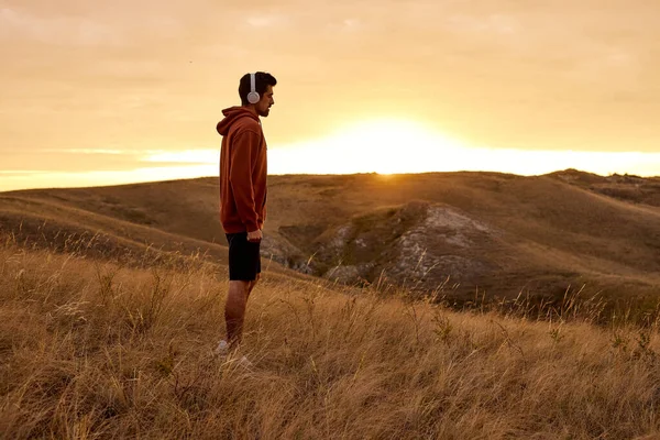 Genießen Sie das Leben. Mann steht auf Bergfeld und genießt den Sonnenaufgang, hört Musik — Stockfoto