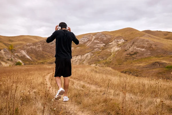 Sportsman είναι το περπάτημα στο πεδίο μεταξύ των βουνών μετά το τζόκινγκ, κάντε ένα διάλειμμα, θέα από πίσω — Φωτογραφία Αρχείου
