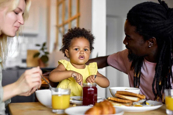 Χαριτωμένο μαύρο κορίτσι παιδί απολαμβάνοντας πρωινό με τους γονείς στο σπίτι, τρώγοντας χυλό — Φωτογραφία Αρχείου