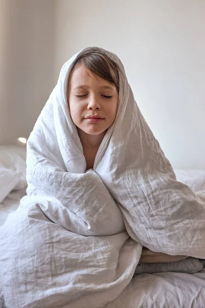 眠い子の男の子は白いベッドで毛布に包まれた。朝だ。リラックスタイム. — ストック写真