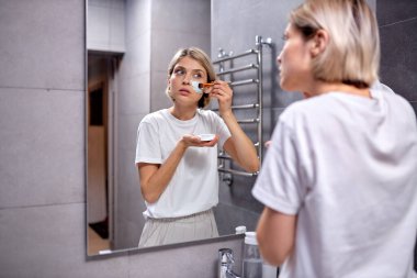 Genç bayan nemlendirilmiş yumuşak, sağlıklı hassas cilde fırçayla maske takıyor.