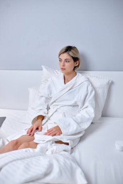 Bornozlu kısa saçlı kadın evde yatakta dinleniyor, dinleniyor.