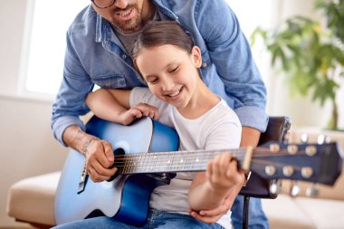 Yakışıklı genç adam küçük tatlı kıza evde gitar çalmayı öğretiyor.
