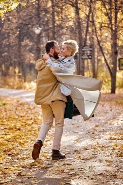Aşıklar sonbahar parkında yürüyor ve sarılıyorlar, birlikte vakit geçirmenin tadını çıkarıyorlar.