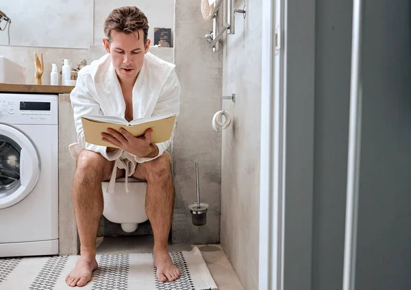 Libro di lettura maschile mentre seduto sulla tazza del water a casa, rilassante, avendo riposo — Foto Stock