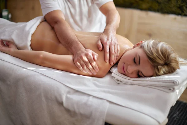Приваблива молода біла жінка розслабляється в спа-центрі, приймаючи масаж спини — стокове фото