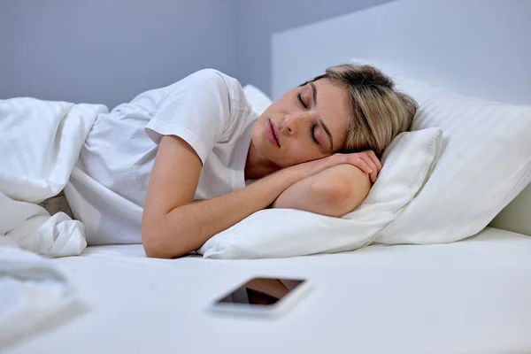 Wanita berbaring di piyama di tempat tidur di kamar tidur. Interior putih bergaya. perempuan jatuh tertidur — Stok Foto