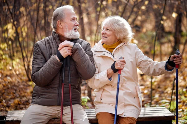 Amigável casal de idosos apaixonados envolvidos na caminhada nórdica no parque, ter descanso — Fotografia de Stock