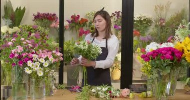 Çiçekçide buket için çiçek düzenleyen genç ve güzel bir asistan..