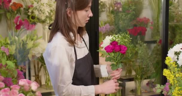 Good-looking floral assistant arranging flowers for bouquet at flower shop. — Stock Video