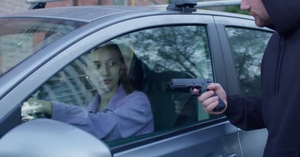 Gevaarlijke crimineel met pistool stelen auto van bange jonge vrouw van buiten, bedreigingen — Stockvideo