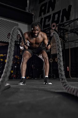 Savaş halatıyla aktif siyah bir adam spor salonunda egzersiz yapıyor.