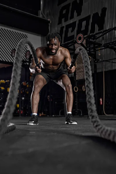 Hombre negro activo con cuerda de batalla haciendo ejercicio en el gimnasio de fitness de entrenamiento funcional — Foto de Stock