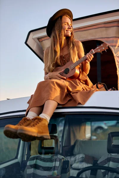 Adorabile signora carina in abito e cappello seduto sulla parte superiore del furgone retrò minig giocare ukulele — Foto Stock