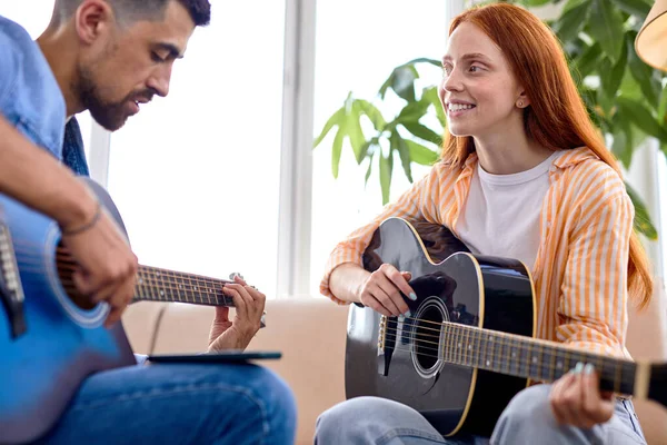 Heureux couple en amour assis sur canapé tandis que jeune homme enseignant petite amie jouer de la guitare — Photo