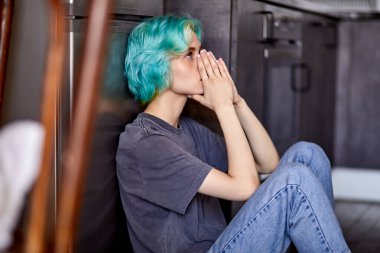 Üzgün bir kadın mutfakta yerde tek başına oturuyor.