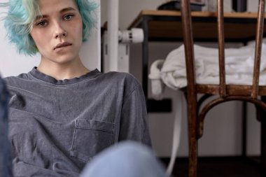 Üzgün, endişeli bir kadın yerde tek başına oturuyor. Yalnızlıktan başı dertte, dudaklarını ısırıyor.