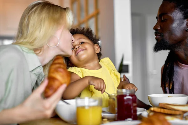 Αγαπημένοι γονείς φιλώντας το κορίτσι παιδί κάθεται πίσω από το τραπέζι κατά τη διάρκεια του πρωινού ή γεύμα — Φωτογραφία Αρχείου