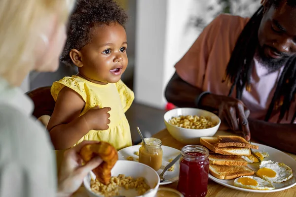 Παιδί τρώει πρωινό. Το παιδί τρώει πόριτζ. Μικρό κορίτσι στο τραπέζι με τους γονείς στην κουζίνα — Φωτογραφία Αρχείου