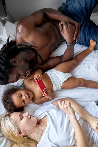 Vista superior de la familia multiétnica madre, padre e hija jugando viendo smartphone — Foto de Stock