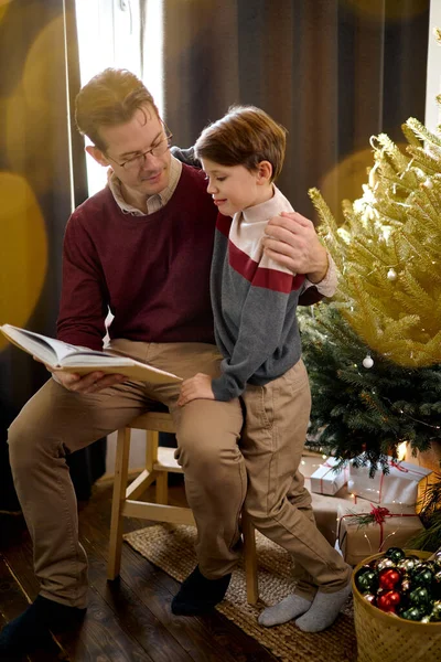 Дружелюбный папа-одиночка с сыном читают сказки отдых праздничное время накануне в уютной комнате — стоковое фото