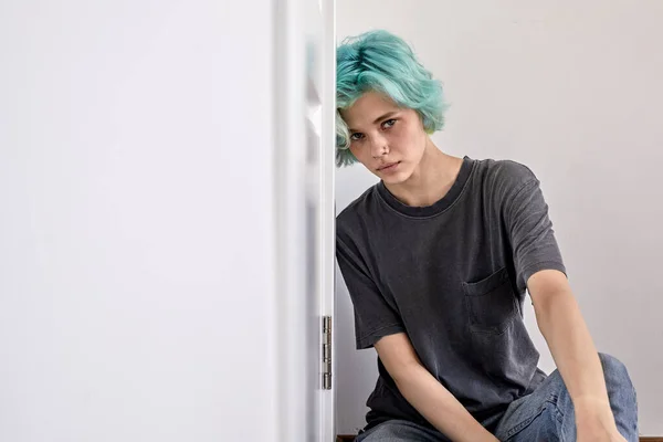 Junge Frau mit grünen Haaren sitzt auf dem Boden an die Wand gelehnt und sieht deprimiert und aufgebracht aus — Stockfoto