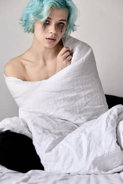 Беспокойная молодая женщина сидит на кровати завернутая в одеяло. Стрессовая женщина дома — стоковое фото