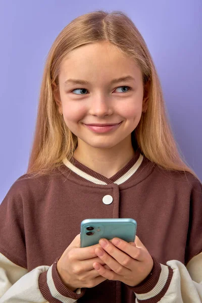 Retrato de encantadora menina doce leitura envio sms para amigos, sorrindo, isolado em roxo — Fotografia de Stock