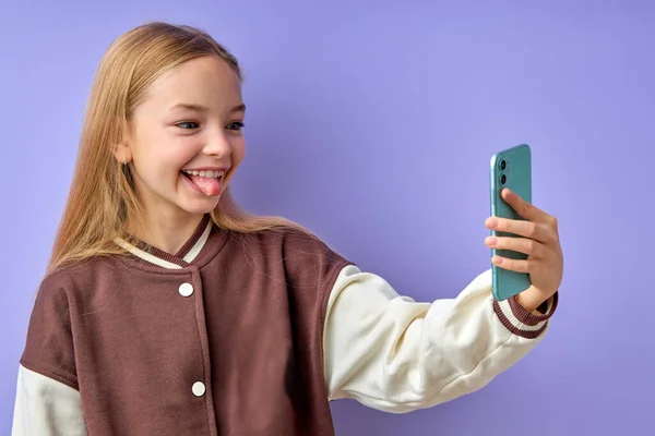 Vrolijk amerikaans meisje doet selfie shot op smartphone, geïsoleerd op paars. — Stockfoto