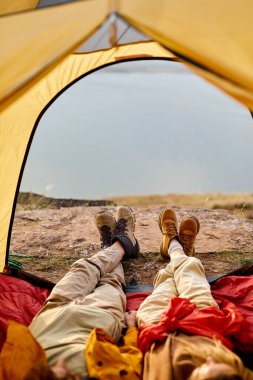 Sonbahar günü göl kenarında kamp yapan ve çadır girişinde uzanan çiftin yüksek açılı görüntüsü.