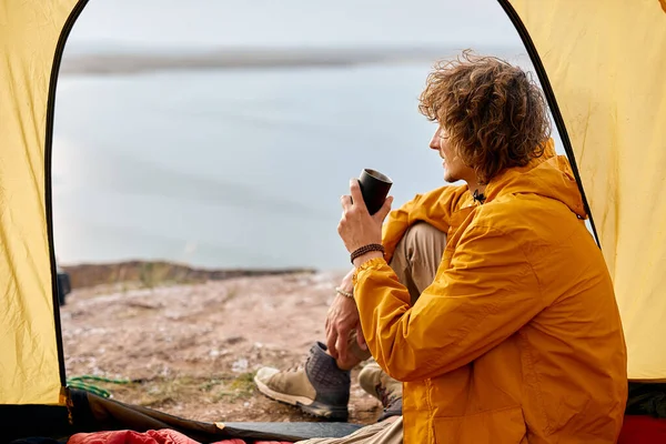 Vista posteriore sul maschio riccio seduto in tenda bere tè o caffè godendo vista paesaggio — Foto Stock