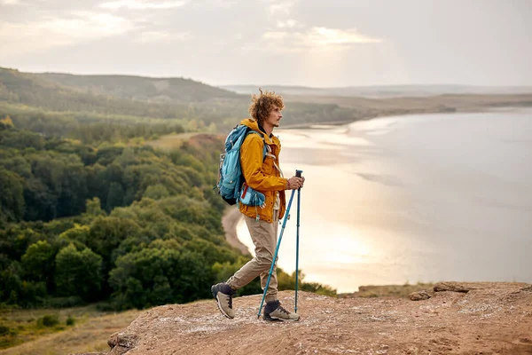 Jovem homem trekking em montanhas tendo relaxante pausa, segurando caminhadas pólos — Fotografia de Stock