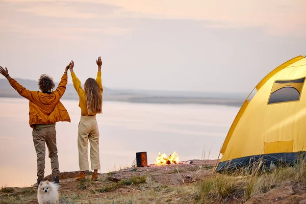 Gölde akşam kampı. Turist çift, kamp ateşinin yanındaki kadın ve erkek, arkadan manzara — Stok fotoğraf