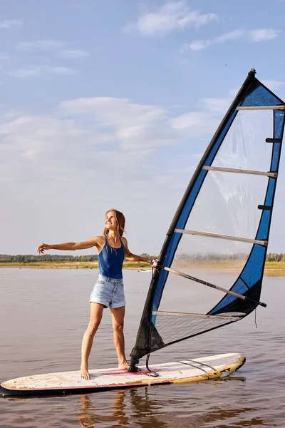 Femme se tient sur la planche à voile et tient la voile. Planche à voile sur l'eau du lac, détente sur l'eau. — Photo