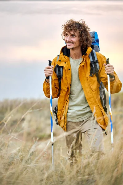 Heyecanlı sportif kıyafetli bir erkek sporcu dağlarda yürüyüş direğiyle yürüyor. — Stok fotoğraf