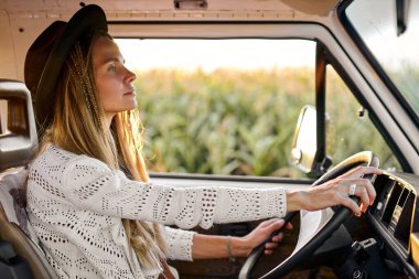 Şapkalı, uzun saçlı, mini minibüslü, mısır tarlasından geçen kadına odaklanmış bir bakış açısı