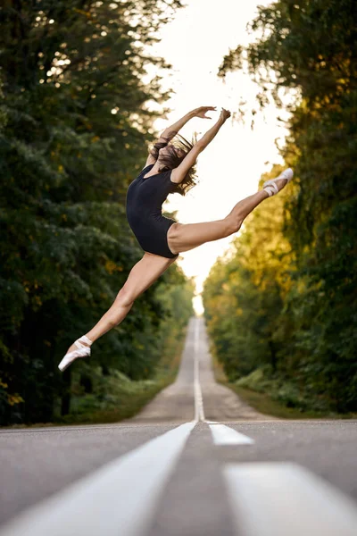 Beyaz tenli çekici balerin günbatımında ormanda atlama eğitimi alıyor. sanat balesi